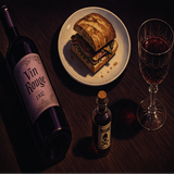 Table setting with lilac wine bottle, a sandwich, a vial of poison and a glass of wine. This Murder Mystery Play intrigues with this poster design